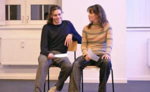 Two students sitting on chairs with scripts in their hands
