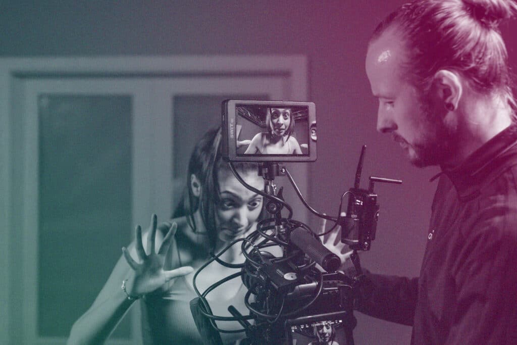 An actor pulls a shocked expression for a camera. This is visible in the cameras monitor where there is also a videographer.