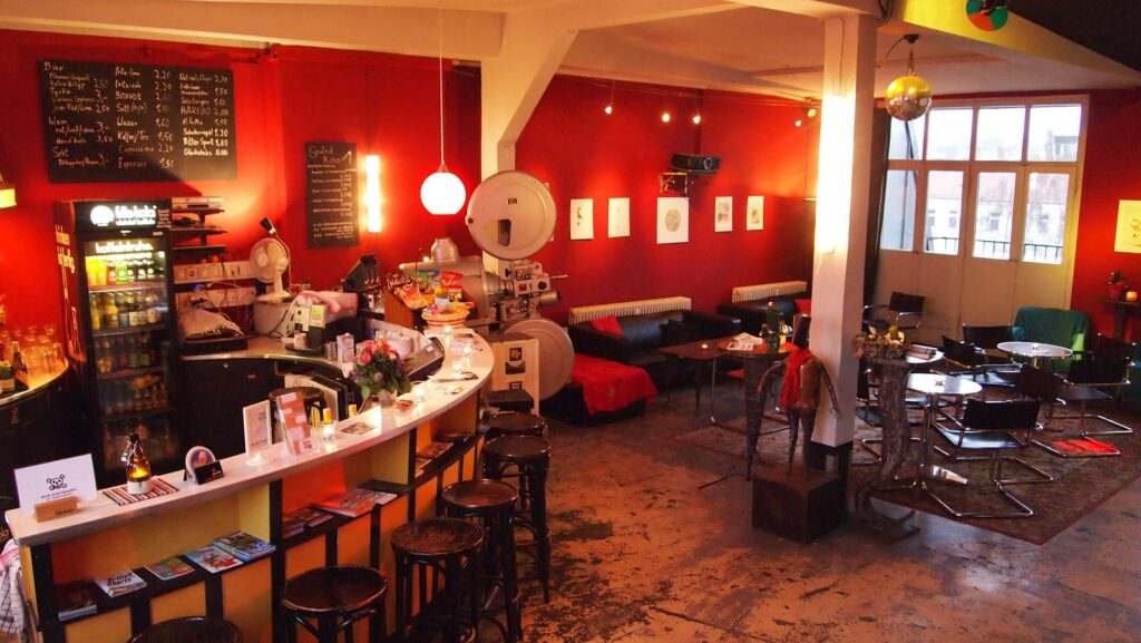 Interior of Sputnik cinema showing the bar and a seating area with sofas and chairs. By the curved bar, there are several barstools, as well as flyers.